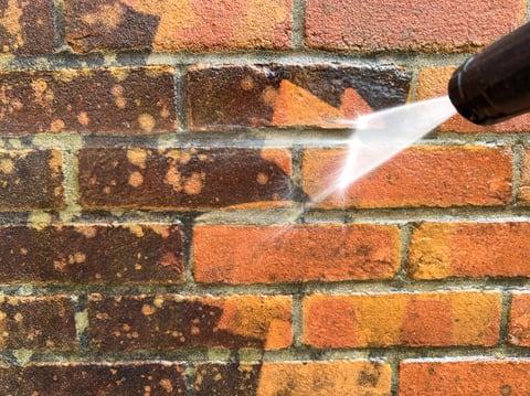 Close up of pressure washer cleaning brick wall