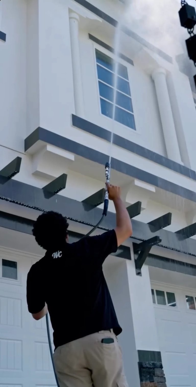 Technician in black shirt installing or adjusting equipment on white modern building facade with blue-trimmed windows